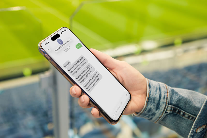 Main tenant un smartphone dans un stade de sport envoyant des SMS à IOLAN SCRC pour activer une connexion cellulaire